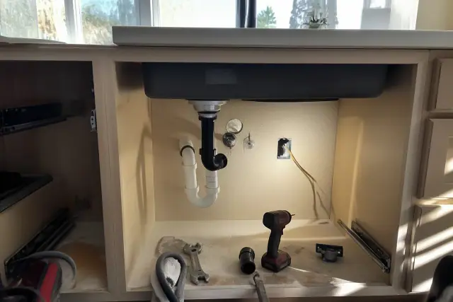 Open plumbing and electrical wiring under a kitchen sink in a Phoenix, AZ home during a garbage disposal repair.