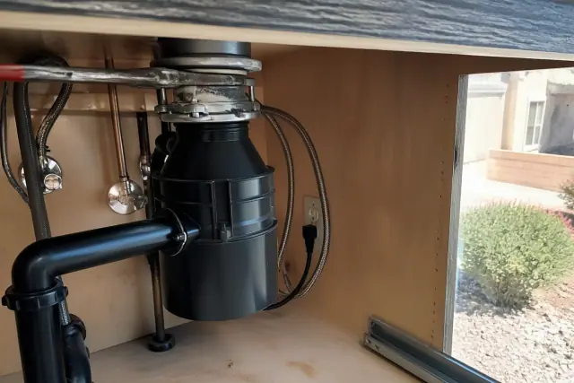 Plumber repairing a garbage disposal with a wrench and pipe putty in a kitchen in Chandler, AZ.