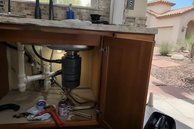 Technician performing garbage disposal repair under a kitchen sink in an Avondale, AZ home.