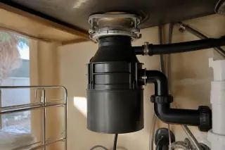 New mounting flange and pipe joints on a repaired garbage disposal under a kitchen sink in Phoenix, AZ.