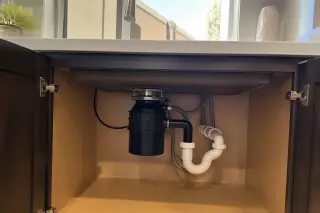 Garbage disposal unit with connected plumbing and electrical wiring under a kitchen sink in a Phoenix, AZ home.
