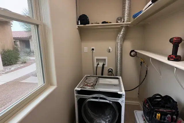 Technician performing a gas dryer inspection in a Phoenix, AZ laundry closet with exposed venting and tools.