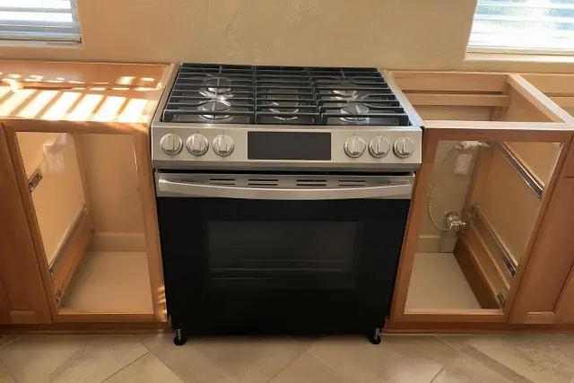 Gas range installed in a kitchen cabinet cutout in Phoenix, AZ, showing connection hoses and leveled positioning.