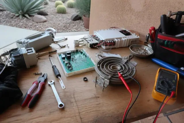 Multimeter testing a dishwasher heating element and control board on a workbench in Phoenix, AZ.