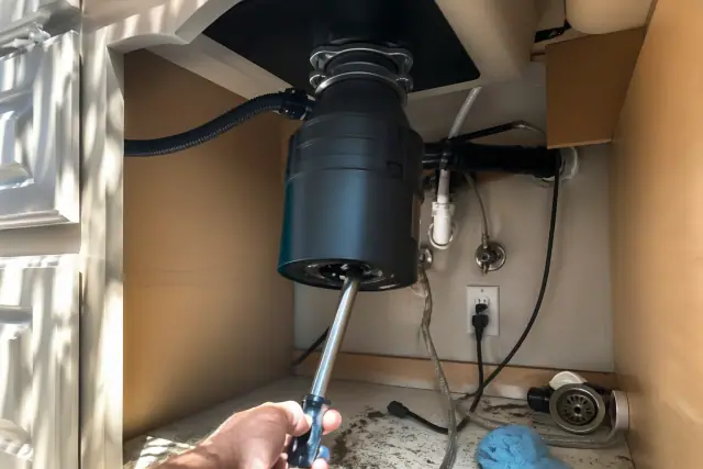 A wrench clearing a jammed garbage disposal unit under a kitchen sink in a Phoenix, AZ home.