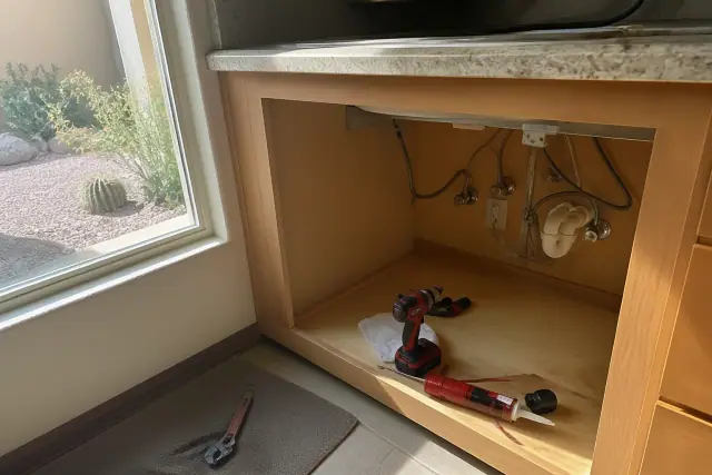 Under-counter area with exposed plumbing and tools during a garbage disposal repair in Phoenix, AZ.