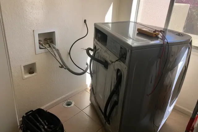 LG washer undergoing repair with a multimeter and exposed hoses in a Phoenix, AZ utility room.