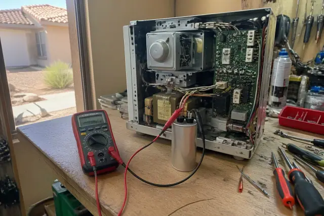 Technician testing a microwave high-voltage capacitor with a multimeter on a workbench in Avondale, AZ.