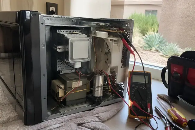 Technician repairing a microwave with exposed interior components and a multimeter in a Tempe, AZ home kitchen.