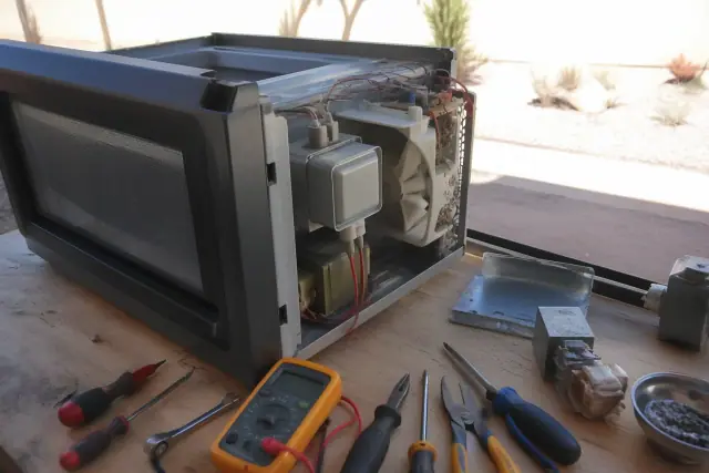 Microwave repair in progress on a wooden workbench with tools and exposed components in a Mesa, AZ workshop.