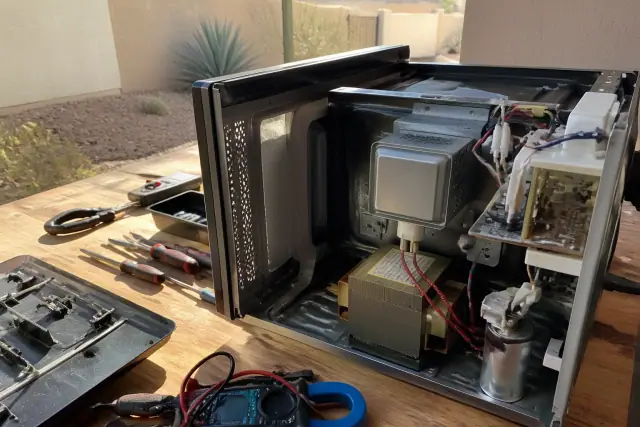 A disassembled microwave on a workshop workbench during a repair job in Glendale, AZ.