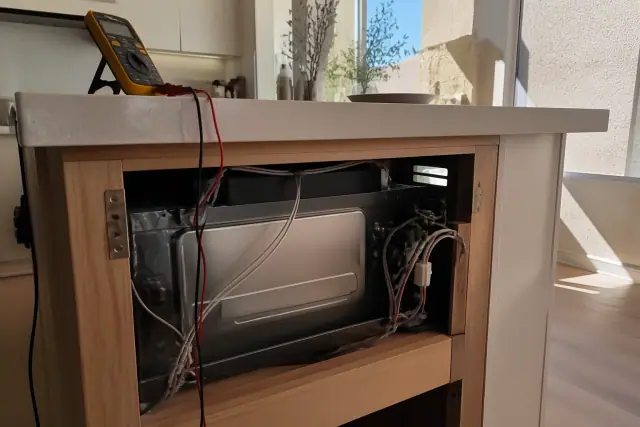 Technician's microwave repair progress on a kitchen island cabinet in Scottsdale, AZ with a multimeter on the edge.