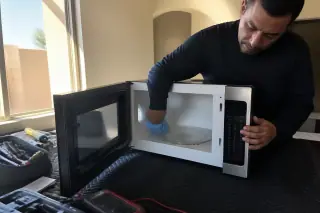 Technician testing the control board of a microwave on a work mat in a Phoenix, AZ home.
