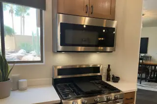 Technician using diagnostic tools on a countertop microwave on a kitchen island in a Phoenix, AZ home.