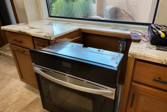 A technician installing a built-in oven into a kitchen cabinet in Paradise Valley, AZ, with tools on the counter.