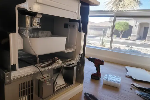 A refrigerator ice maker undergoing repair in a kitchen island in Phoenix, AZ, with a desert view through the window.