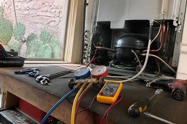 Refrigerator compressor repair on a workbench with testing tools in Tempe, AZ.