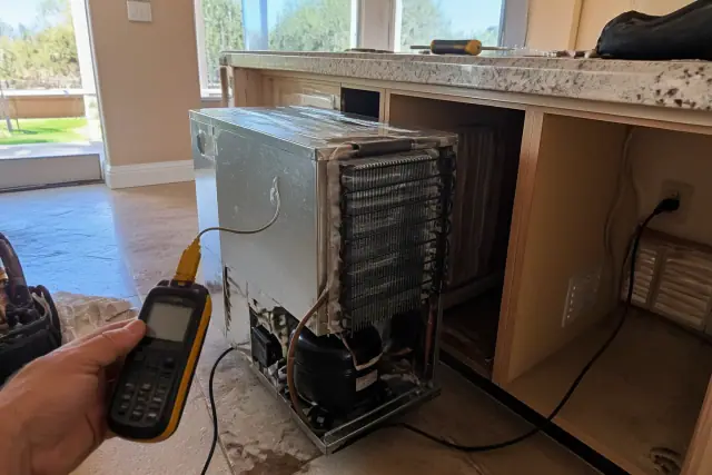 Technician repairing a refrigerator with tools in a kitchen in Gilbert, AZ.