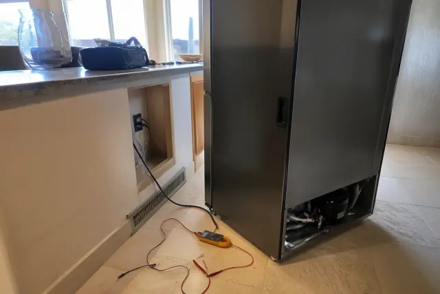 Technician using a multimeter to repair a refrigerator in a kitchen in Phoenix, AZ.