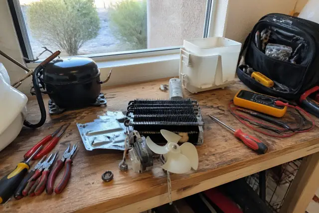 Wooden workbench with refrigerator repair tools and mechanical parts at a home in Goodyear, AZ.