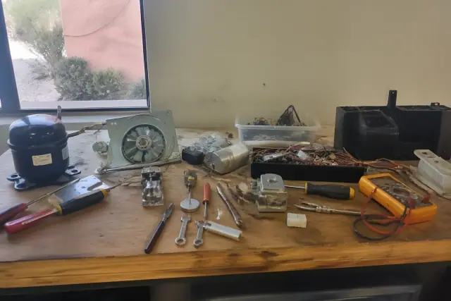 A workbench in Peoria, AZ covered with tools and disassembled refrigerator parts near a window with desert views.