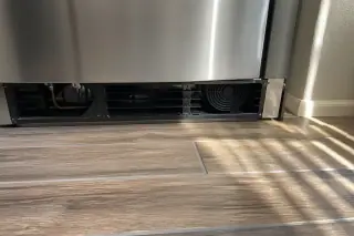 Clean condenser coils and cooling fan inside a stainless steel refrigerator in a Phoenix, AZ kitchen.