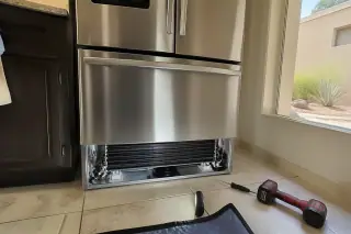 Cleaned condenser coils and cooling fan at the base of a stainless steel refrigerator in a Phoenix, AZ home.