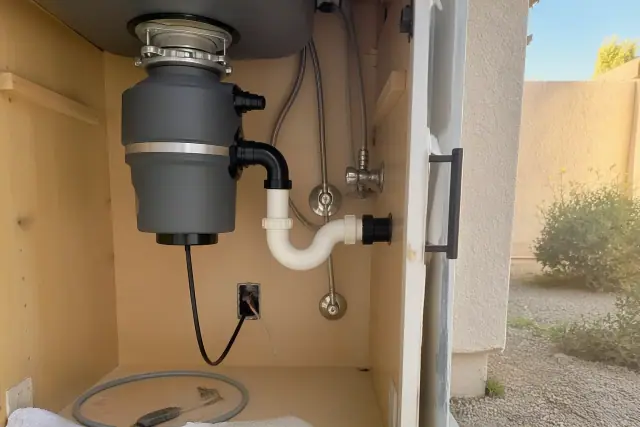New garbage disposal installed under a kitchen sink in Phoenix, AZ, with visible plumbing and wiring.