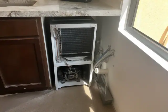 Technician repairing an ice maker with exposed coils in a kitchen in Phoenix, AZ.