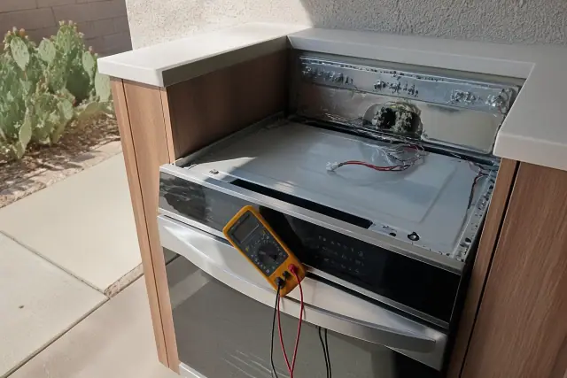 Technician repairing a stove and range in a kitchen in Mesa, AZ, with a multimeter resting on the appliance door.