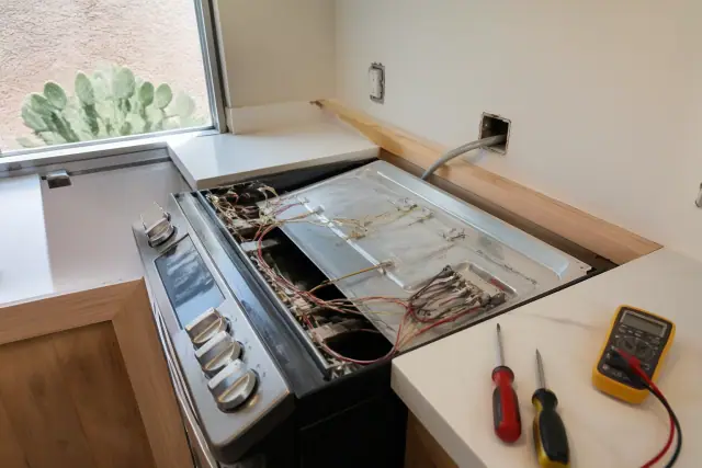 Technician repairing a stove in a Tempe, AZ home kitchen with tools on the counter.