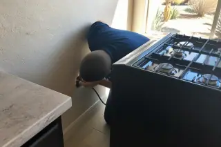 Technician verifying gas and electrical connections behind a freestanding stove in a Phoenix, AZ kitchen.