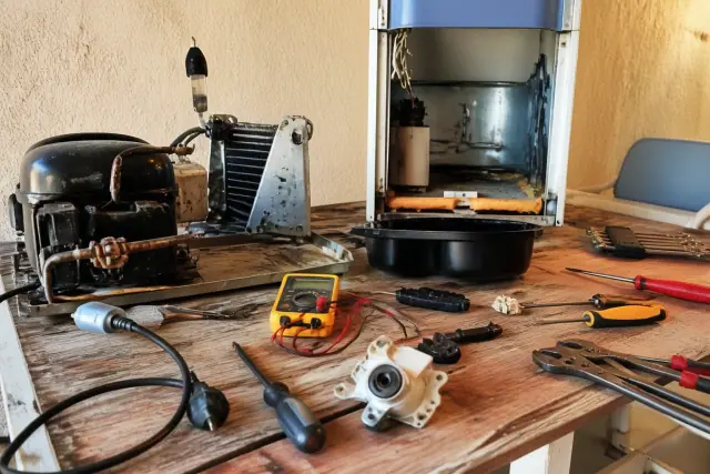 Technician diagnosing a disassembled refrigerator on a workbench in Phoenix, AZ.