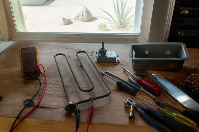 Multimeter connected to an oven heating element during a repair on a wooden workbench in Phoenix, AZ.