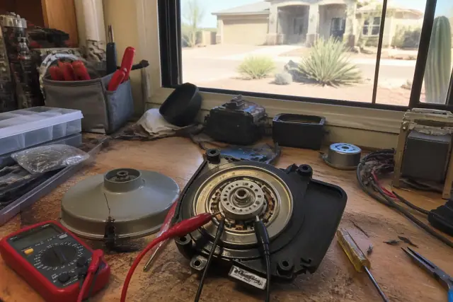 Microwave turntable motor being tested with a multimeter on a cluttered workbench in Phoenix, AZ.