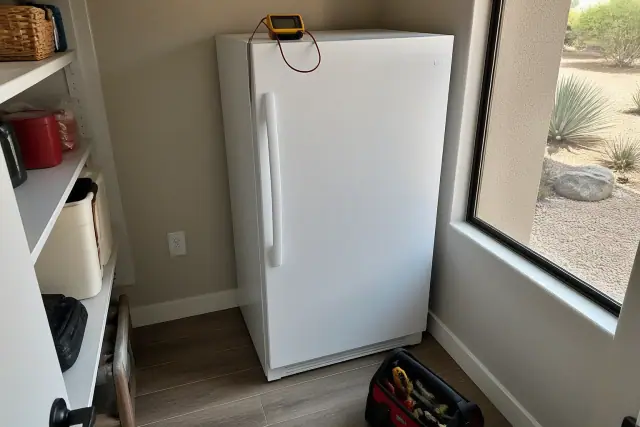 Upright freezer in a Phoenix, AZ pantry with a multimeter on top and a small tool kit on the floor.