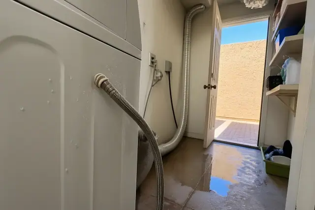 Leaking washer supply hose connection with water on the floor in a laundry closet in Phoenix, AZ.