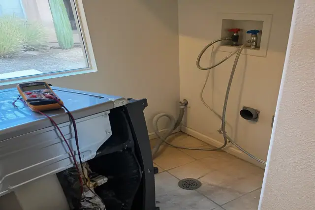 A washing machine pulled out for repairs with exposed hoses and a multimeter in a Peoria, AZ utility room.