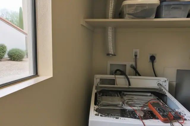 A technician performing a washer repair in a laundry closet in Goodyear, AZ, with internal components exposed.