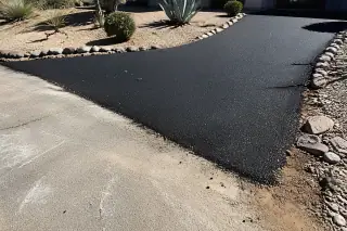 Newly paved residential driveway apron transition at a road edge in Phoenix, AZ, with desert agave and gravel landscaping.