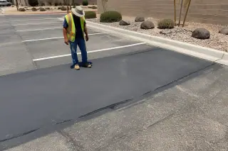 Worker inspecting a freshly sealed asphalt patch in a retail parking lot in Phoenix, AZ.