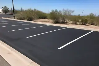 Freshly paved asphalt parking stalls with clear white striping and desert creosote bushes in Phoenix, AZ.