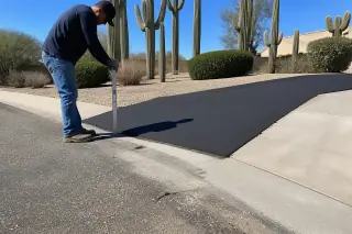 Contractor using a straightedge to check a new asphalt driveway transition in Phoenix, AZ.