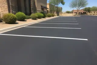 Smooth black asphalt parking stalls with white lines and desert foliage in Phoenix, AZ.