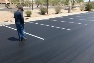 Service professional inspecting a freshly sealcoated parking lot surface under harsh sunlight in Phoenix, AZ.