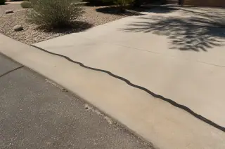 Rubberized asphalt sealant filling a crack in a driveway apron transition in Phoenix, AZ, with creosote bushes.