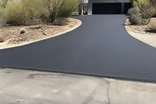 Smooth asphalt driveway apron meeting a residential road in Phoenix, AZ, with surrounding desert scrub vegetation.