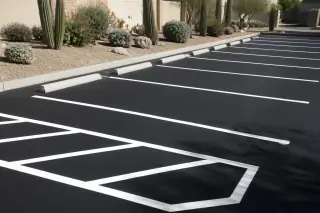 Freshly painted parking stall lines on new black asphalt with desert gravel and cacti in Phoenix, AZ.
