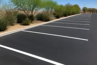 Crisp white parking stall lines painted on new asphalt with palo verde trees in the background in Phoenix, AZ.