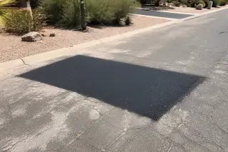 Rectangular asphalt utility patch in a residential road in Phoenix, AZ, surrounded by desert gravel.